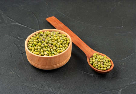 Green mung beans in wooden bowl and spoon on dark backgroundの写真素材