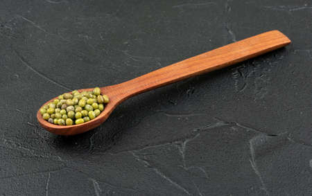 Green mung beans in a wooden spoon on a dark backgroundの写真素材