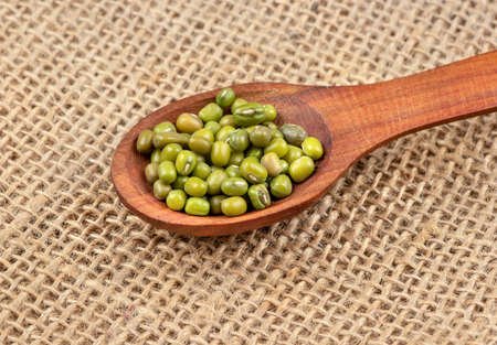 Wooden spoon with green mung beans close-up on burlapの写真素材