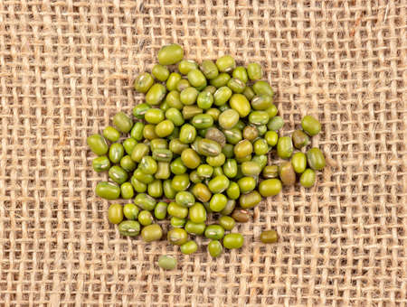 Pile of raw green mung grains scattered on burlap, top viewの写真素材