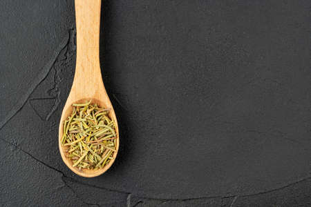 Small wooden spoon with dry rosemary close-up on dark backgroundの写真素材