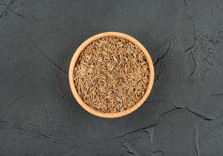 Dry cumin in a wooden bowl on a dark background, top viewの写真素材