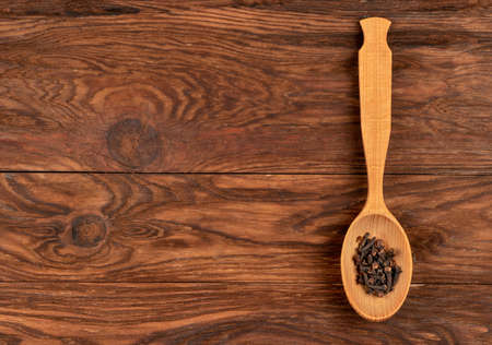 Seasoning dry cloves in a spoon on an empty wooden background, top viewの写真素材