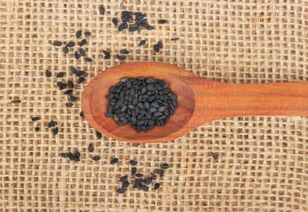 Spoon with black sesame seeds on burlap closeupの写真素材