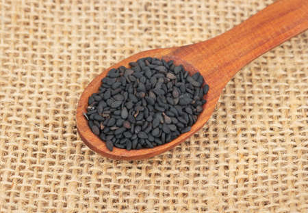 Spoon with black sesame seeds on burlap closeupの写真素材