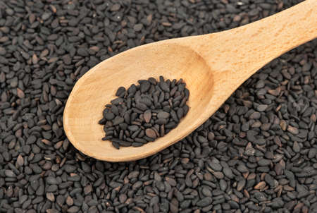 Pile of scattered black sesame seeds with a wooden spoon close upの写真素材