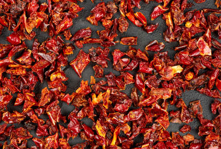Scattered pieces of dry red pepper on a dark background, top view
