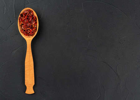 Pieces of dry red pepper in a spoon on an empty dark background, top viewの写真素材