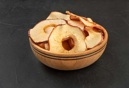 Apple chips in a wooden bowl on a dark backgroundの写真素材