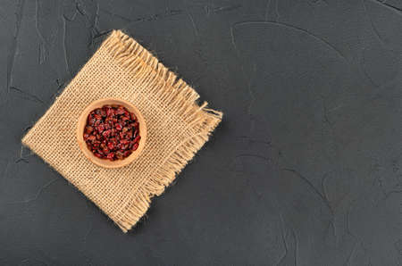 Dry barberry in a wooden bowl on burlap and empty dark background, top viewの写真素材