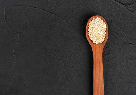 Sesame seeds in a wooden spoon on an empty concrete background, top viewの写真素材