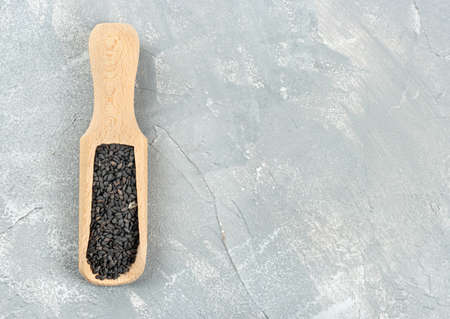 Black sesame in a wooden scoop on a light concrete background, top viewの写真素材