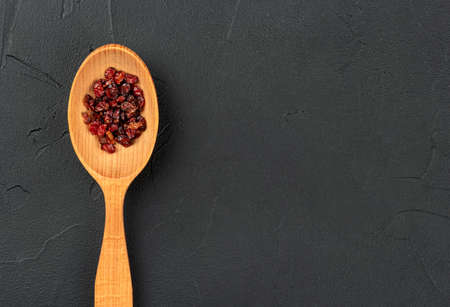 Dry barberry in a wooden spoon on an empty dark backgroundの写真素材