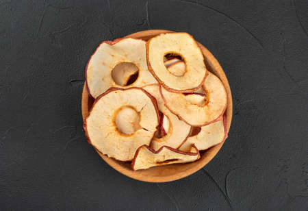 Apple chips in a wooden bowl on a dark background, top viewの写真素材