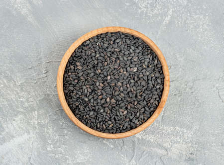 Black sesame seeds in a wooden bowl on a light background, top viewの写真素材