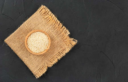 Sesame seeds in wooden bowl on burlap and dark background, top viewの写真素材