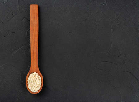 Sesame seeds in a wooden spoon on an empty dark background, top view