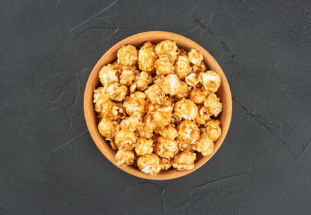 Caramel popcorn in wooden bowl on dark background, top viewの写真素材