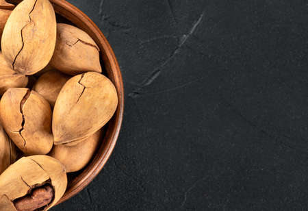 Part of a bowl with in-shell pecans on an empty dark background under the text.