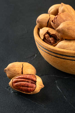 Part of a wooden bowl with in-shell pecans close-up on a dark concrete background.