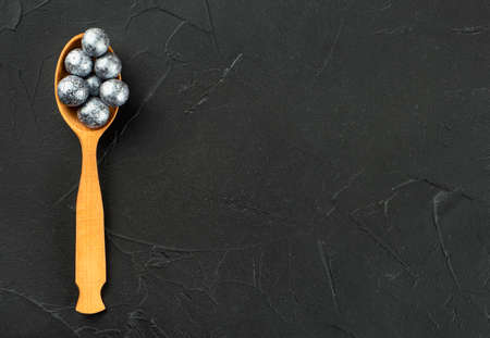Wooden spoon with candy hazelnuts in chocolate on a dark concrete background copy space.の写真素材