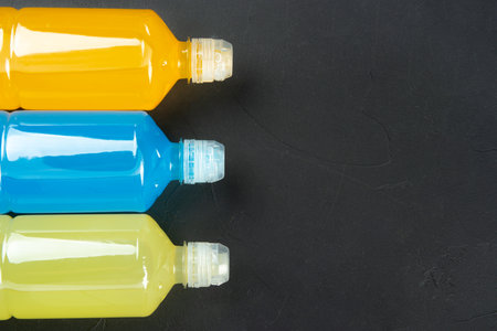 Plastic bottles with blue, orange and lemon isotonic drinks on a dark concrete background, copy space, closeup.の写真素材