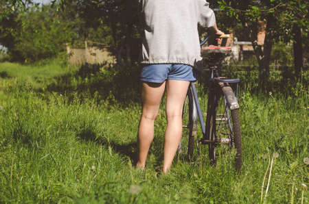 The girl drives an old bicycle on a country road overgrown with grass.の写真素材