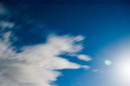 Clouds float in the night sky under moonlight.の写真素材