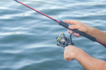 Fisherman's hands with spinning on the background of water.の写真素材