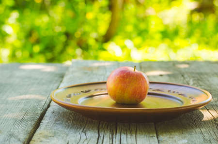 Red apple in a clay bowl on wooden table.の写真素材