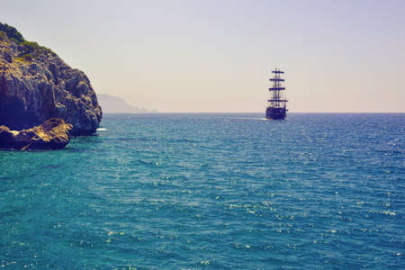 A ship floating in the sea and rocky shore.