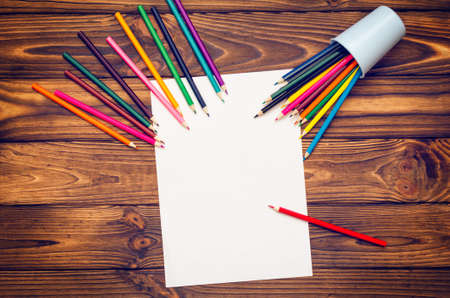 Blank paper and colored pencils on a wooden table.
