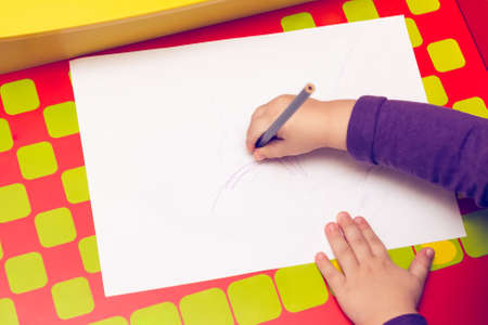On the red table, children's hands with colored pencils and a blank sheet of paper.の写真素材