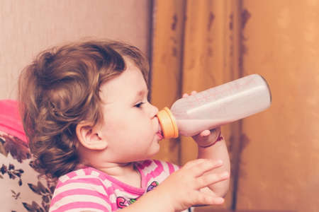 Little girl drinks milk from a bottle.の写真素材