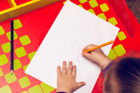 On the red table, children's hands with colored pencils and a blank sheet of paper.の写真素材