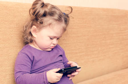 Little girl playing smartphone sitting on sofa.の写真素材