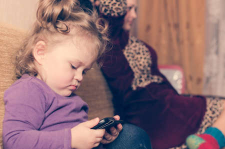 A little girl without parents' attention looks at the smartphone.