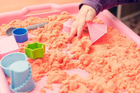 The hands of a child playing with kinetic sand.