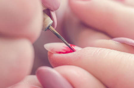 Manicurist paints nails with red lacquer in the salon.