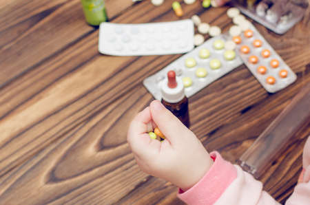 Children's hands with medicines on a wooden table. A small child left unattended plays dangerous drugs.の写真素材