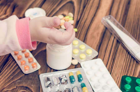 Children's hands with medicines on a wooden table. A small child left unattended plays dangerous drugs.の写真素材