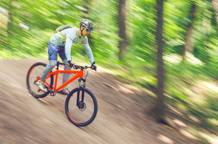 A cyclist in a helmet descends from the mountain on an orange bicycle, motion blur.