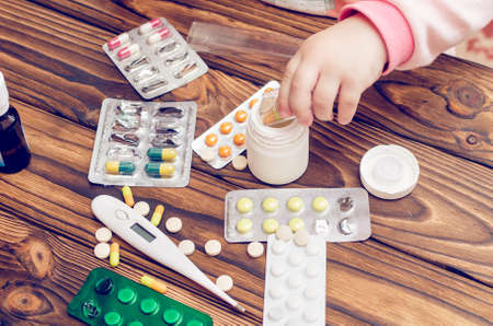 Children's hands with medicines on a wooden table. A small child left unattended plays dangerous drugs.の写真素材