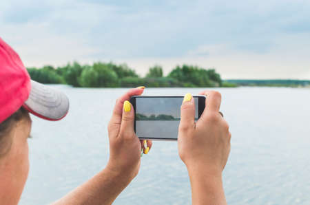 A girl takes pictures of a lake on a mobile phone camera.の写真素材