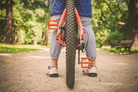 The legs of a cyclist and part of a bicycle on a dirt road, toned.