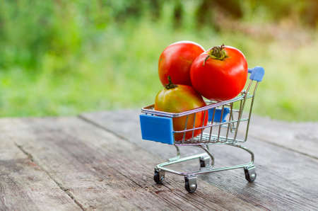 A small shopping trolley with red tomatoes on an old wooden table.の写真素材