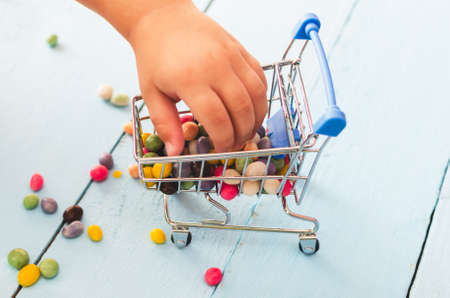 Hands of a child holding a shopping cart with colored sweets on a blue background.の写真素材