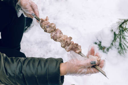 Women's hands strung meat on a skewer in the winter forest.の写真素材