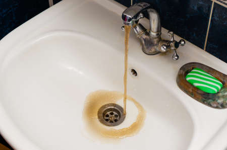 Dirty rusty water flows into a white sink.