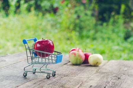 Small shopping trolley with ripe red apple on old wooden table.の写真素材